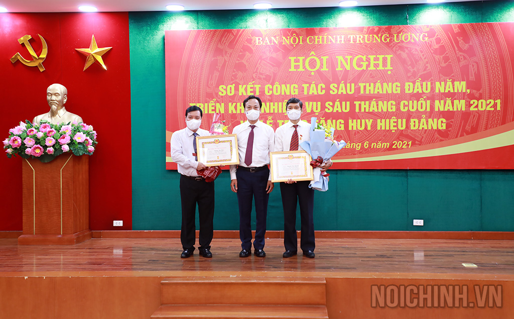 Đồng chí Lại Xuân Lâm, Phó Bí thư Đảng ủy Khối các cơ quan Trung ương tặng hoa chúc mừng 2 đồng chí nhận Huy hiệu 30 năm tuổi Đảng
